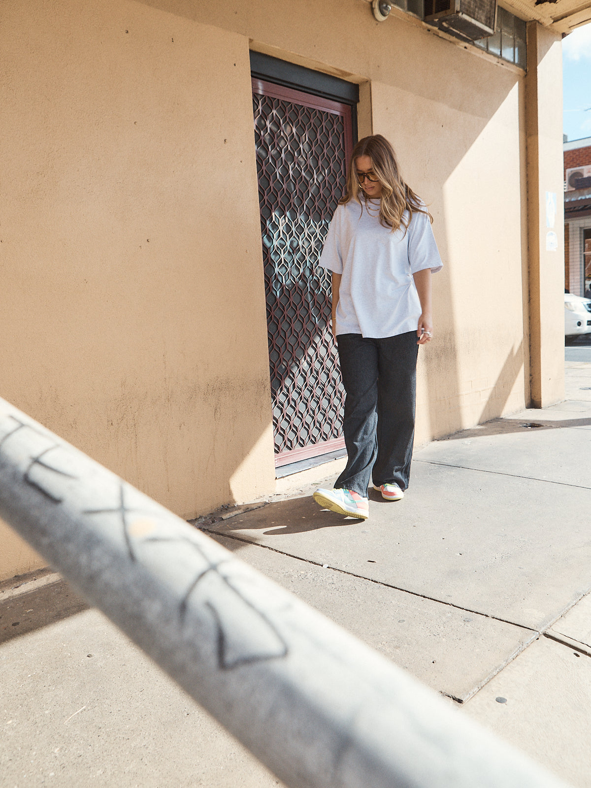 Woman wearing unisex oversized grey marle t-shirt with wide-leg jeans and colourful sneakers.