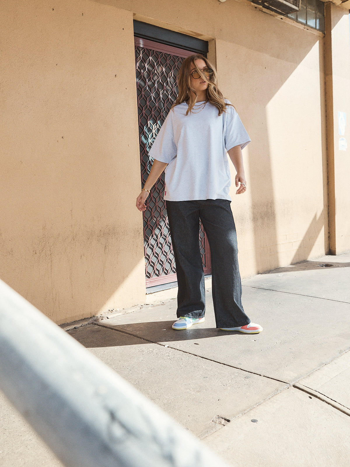 Woman wearing unisex oversized grey marle t-shirt with wide-leg jeans and colourful sneakers.