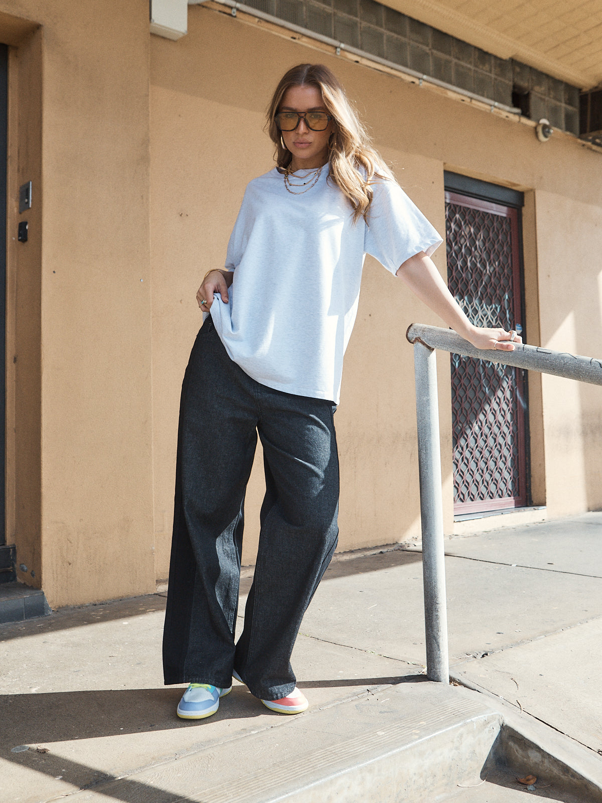 Woman wearing unisex oversized grey marle t-shirt with wide-leg jeans and colourful sneakers.