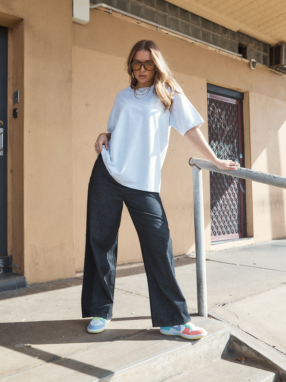 Woman wearing unisex oversized grey marle t-shirt with wide-leg jeans and colourful sneakers.