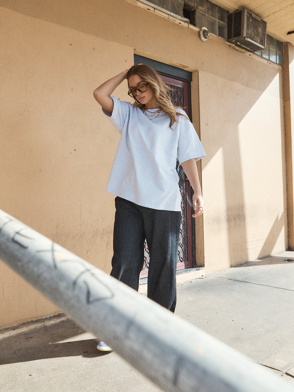 Woman wearing unisex oversized grey marle t-shirt with wide-leg jeans and colourful sneakers.