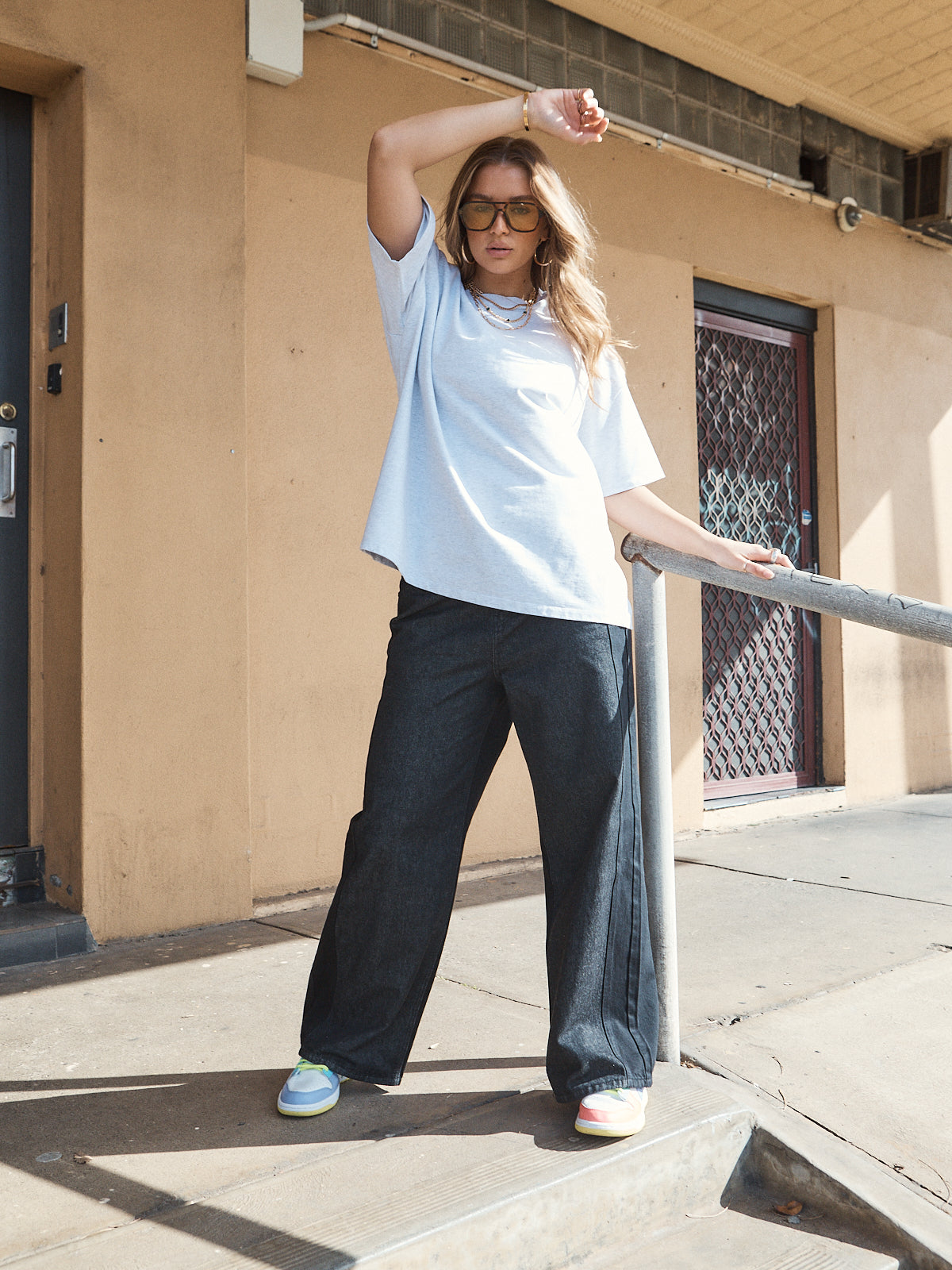 Woman wearing unisex oversized grey marle t-shirt with wide-leg jeans and colourful sneakers.
