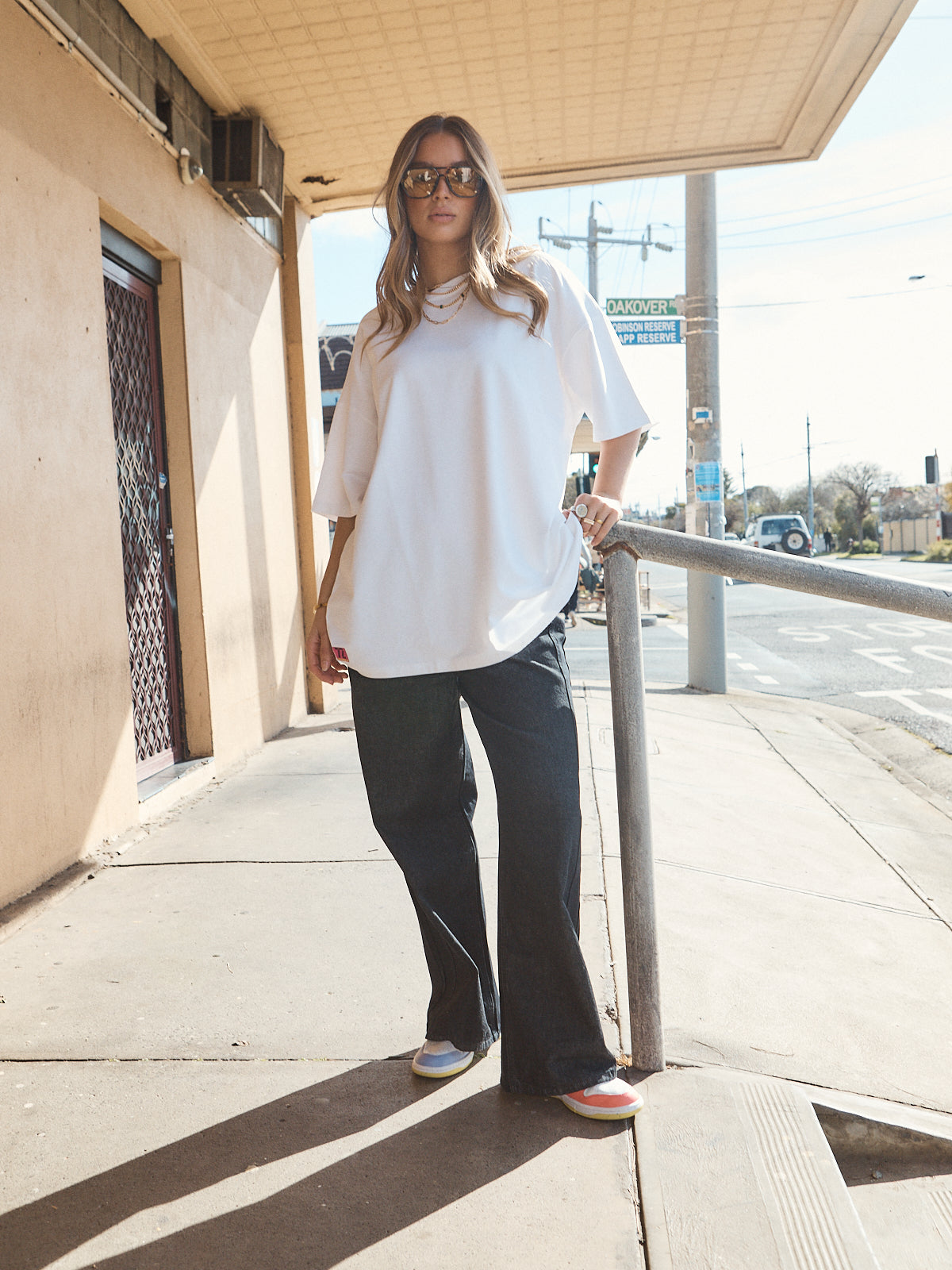 Woman in unisex oversized snow white t-shirt styled with wide-leg black denim and casual sneakers.
