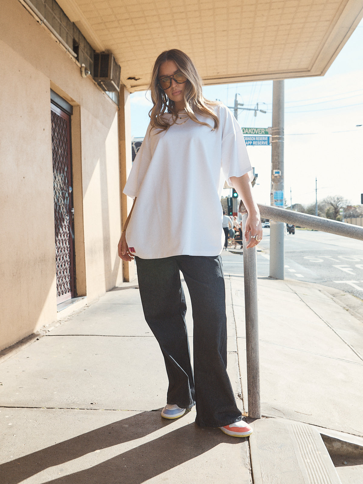 Woman in unisex oversized snow white t-shirt styled with wide-leg black denim and casual sneakers.