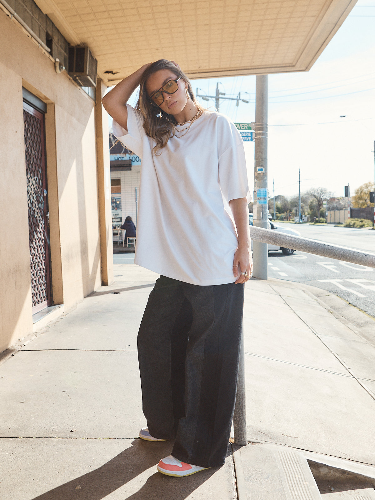 Woman in unisex oversized snow white t-shirt styled with wide-leg black denim and casual sneakers.