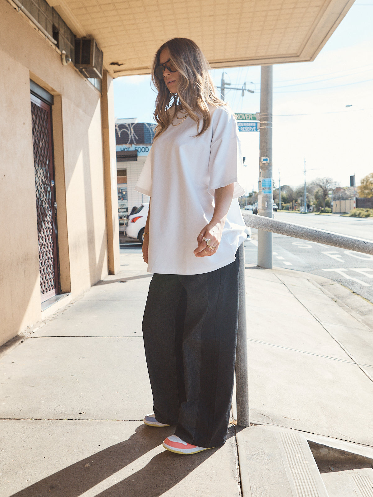 Woman in unisex oversized snow white t-shirt styled with wide-leg black denim and casual sneakers.