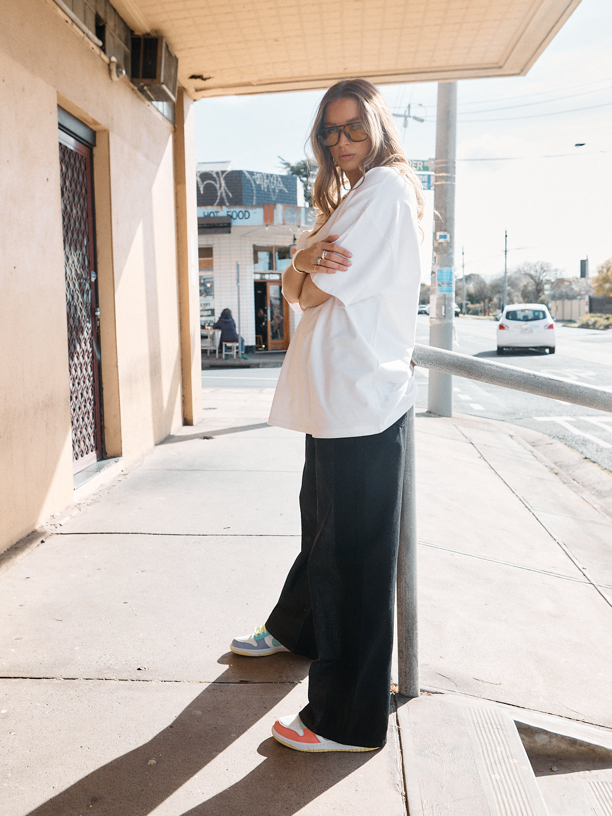 Woman in unisex oversized snow white t-shirt styled with wide-leg black denim and casual sneakers.