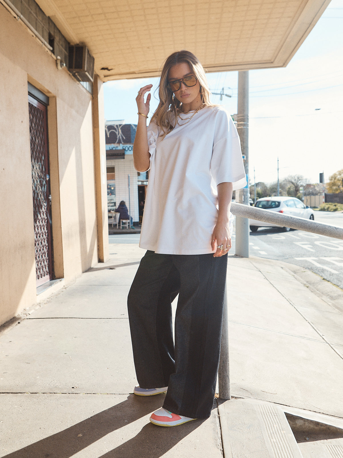 Woman in unisex oversized snow white t-shirt styled with wide-leg black denim and casual sneakers.