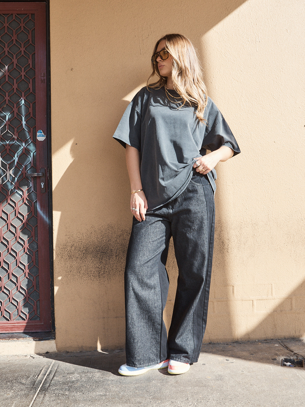 Woman wearing unisex oversized washed black t-shirt styled with wide-leg denim jeans and sneakers.