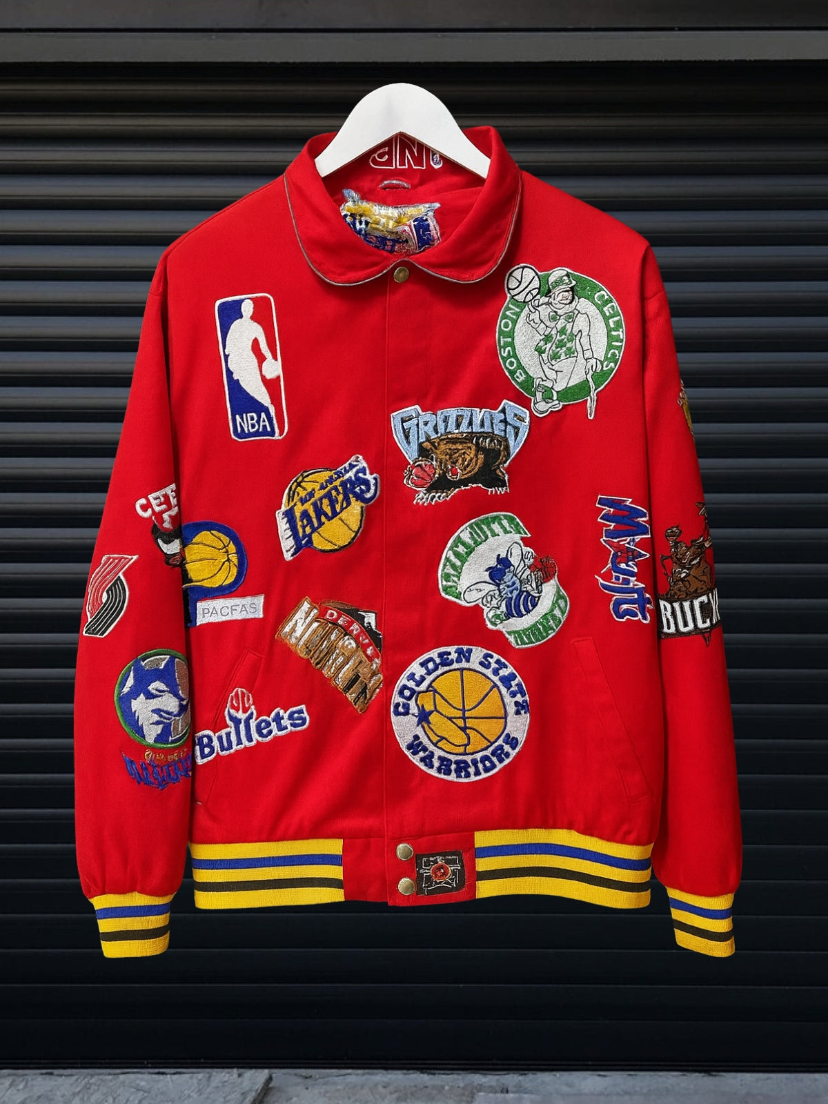 Vintage Red NBA patch jacket with shirt collar and red striped hem featuring team logos including Lakers, Clippers, Bucks, Suns, 76ers, Magic and more, hanging on hanger