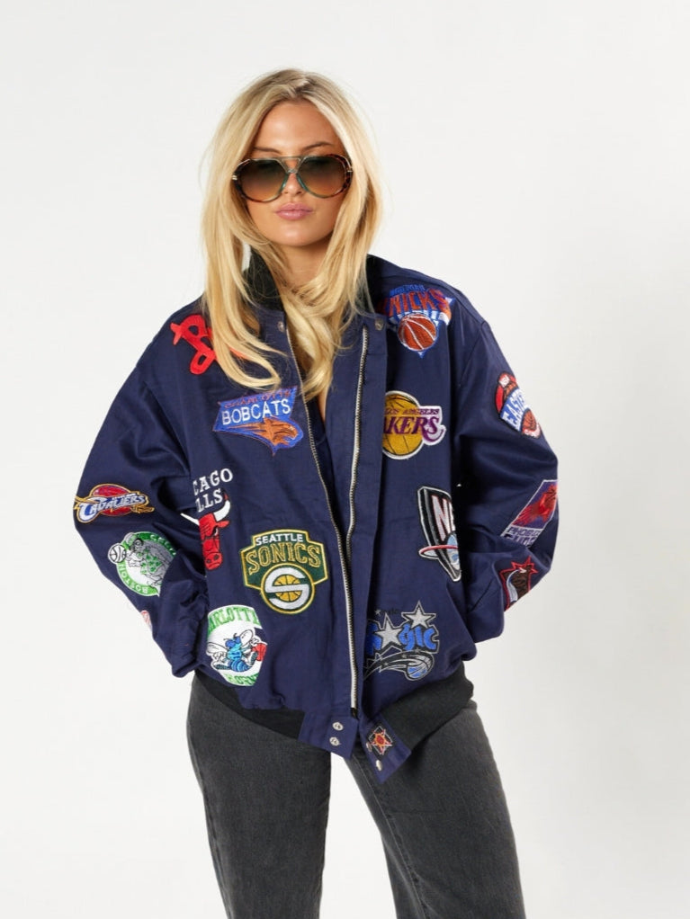 Person wearing a navy blue jacket with various patches on a white background