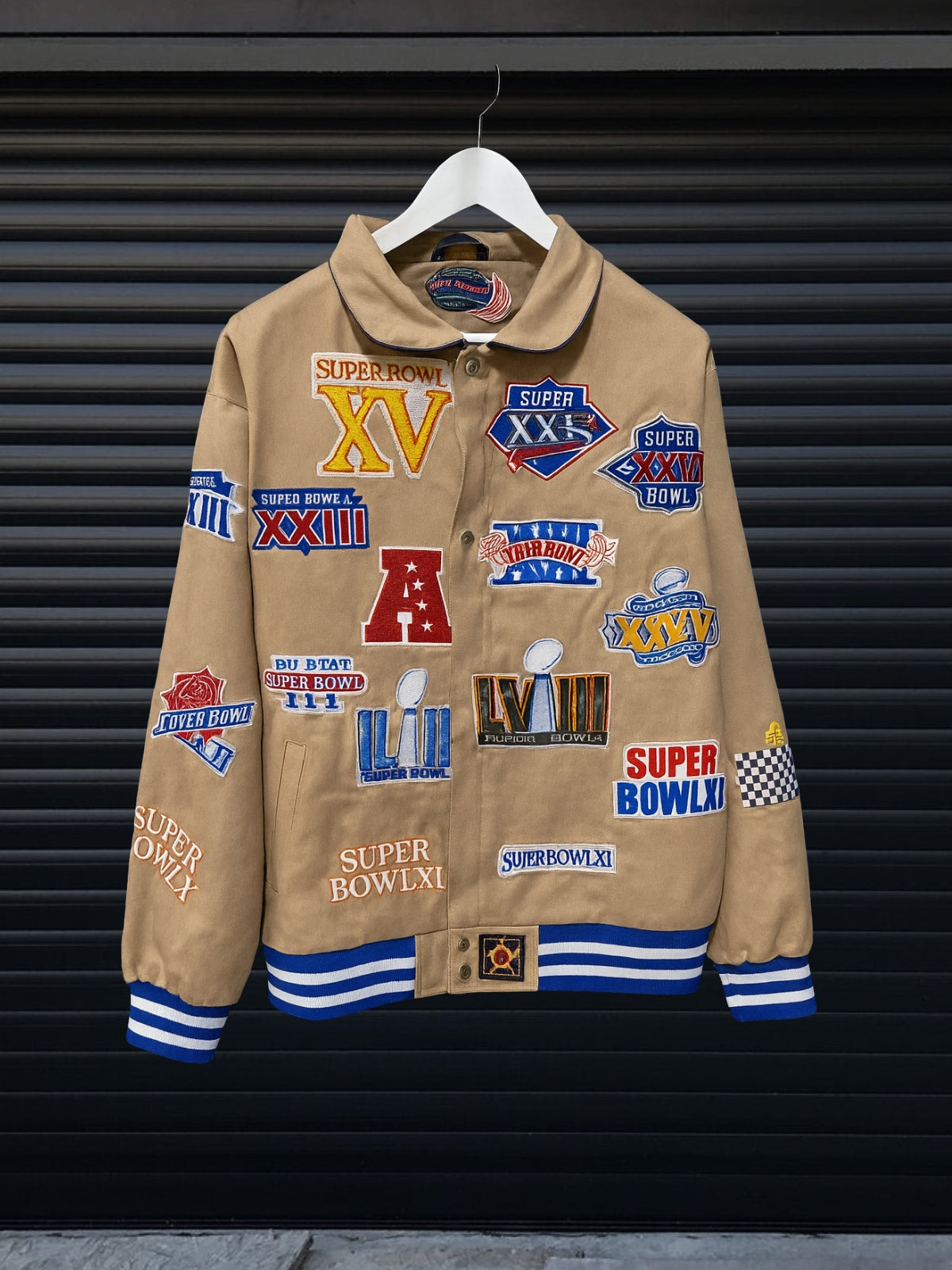Vintage khaki NBA patch jacket with shirt collar and red striped hem featuring team logos including Lakers, Clippers, Bucks, Suns, 76ers, Magic and more, hanging on hanger