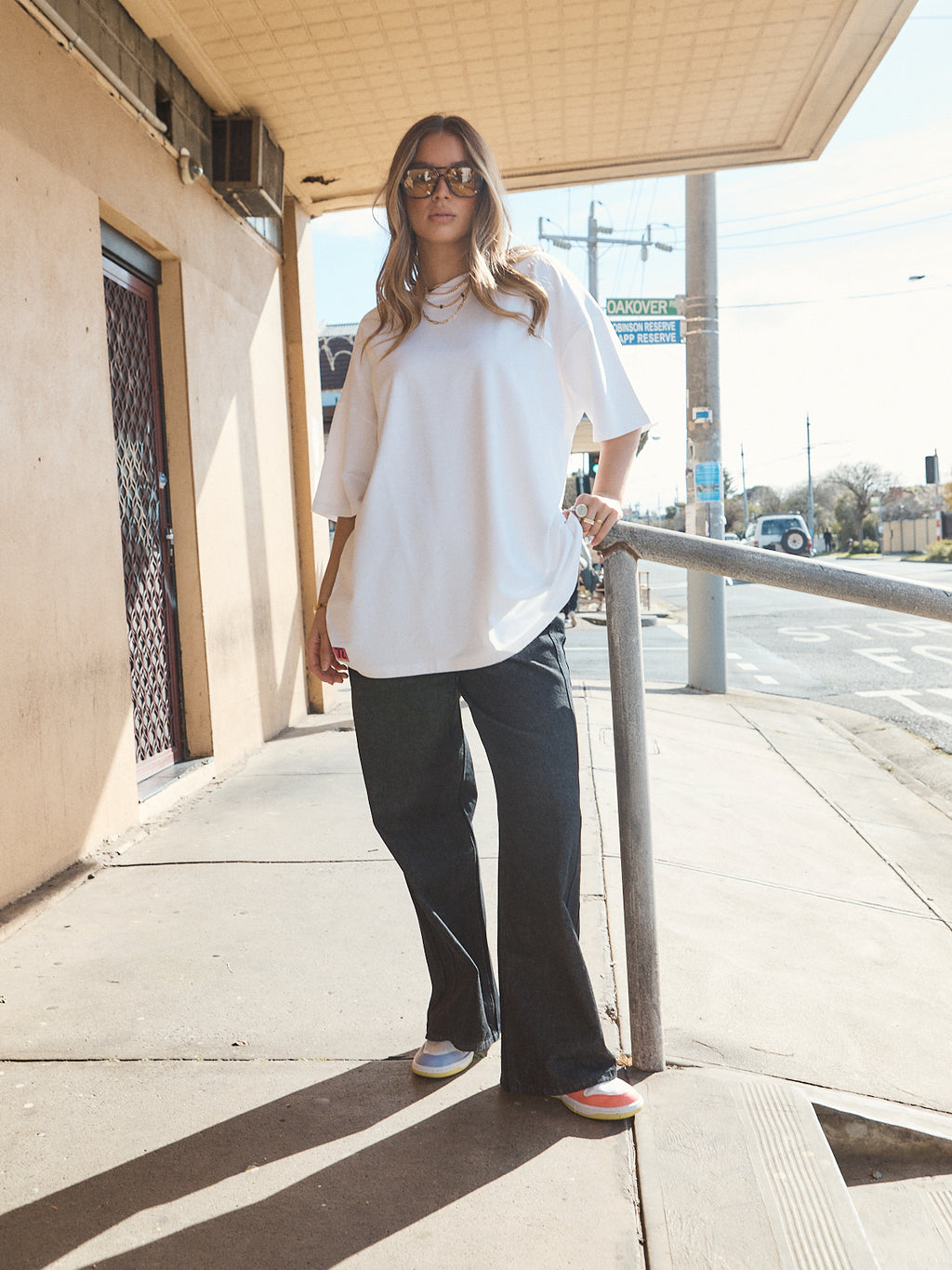 Woman in unisex oversized snow white t-shirt styled with wide-leg black denim and casual sneakers.