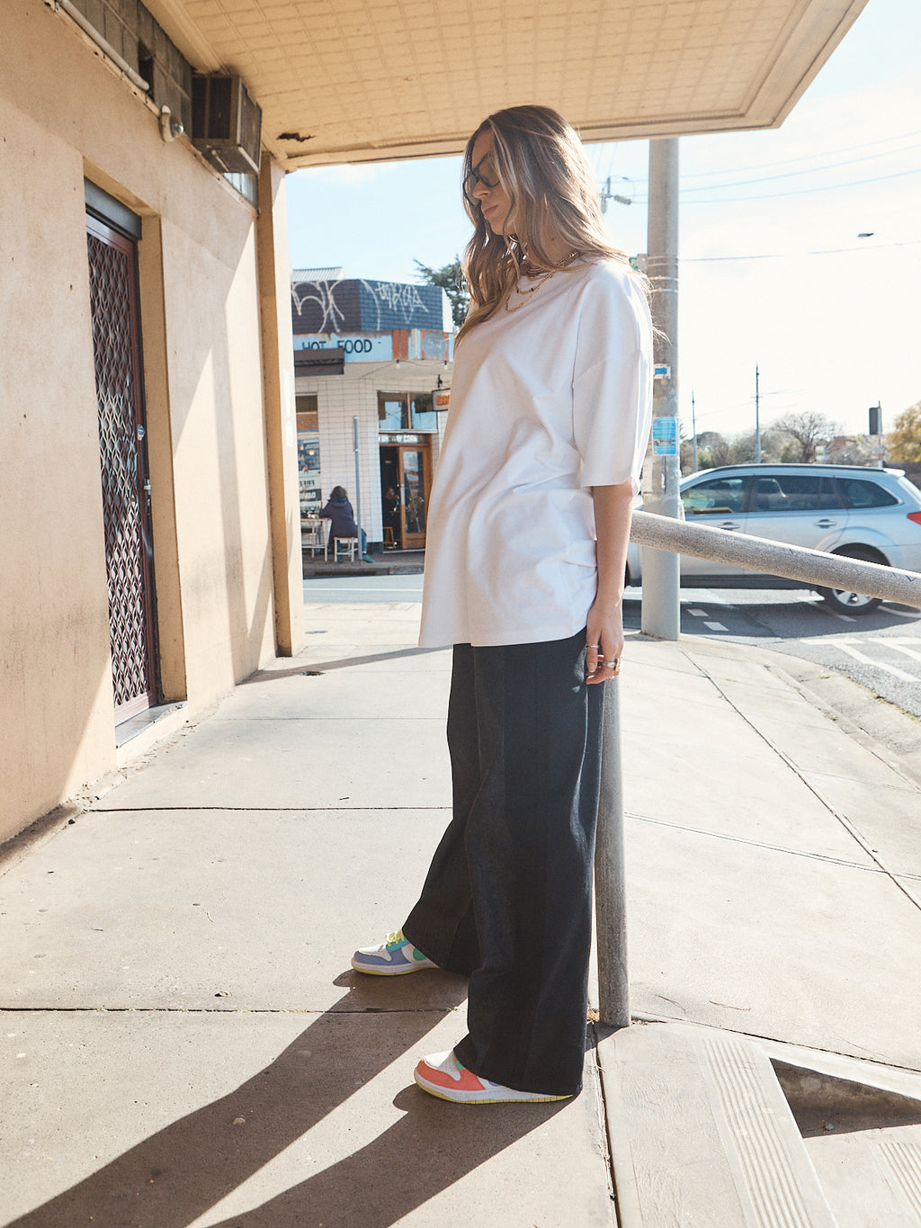 Woman in unisex oversized snow white t-shirt styled with wide-leg black denim and casual sneakers.