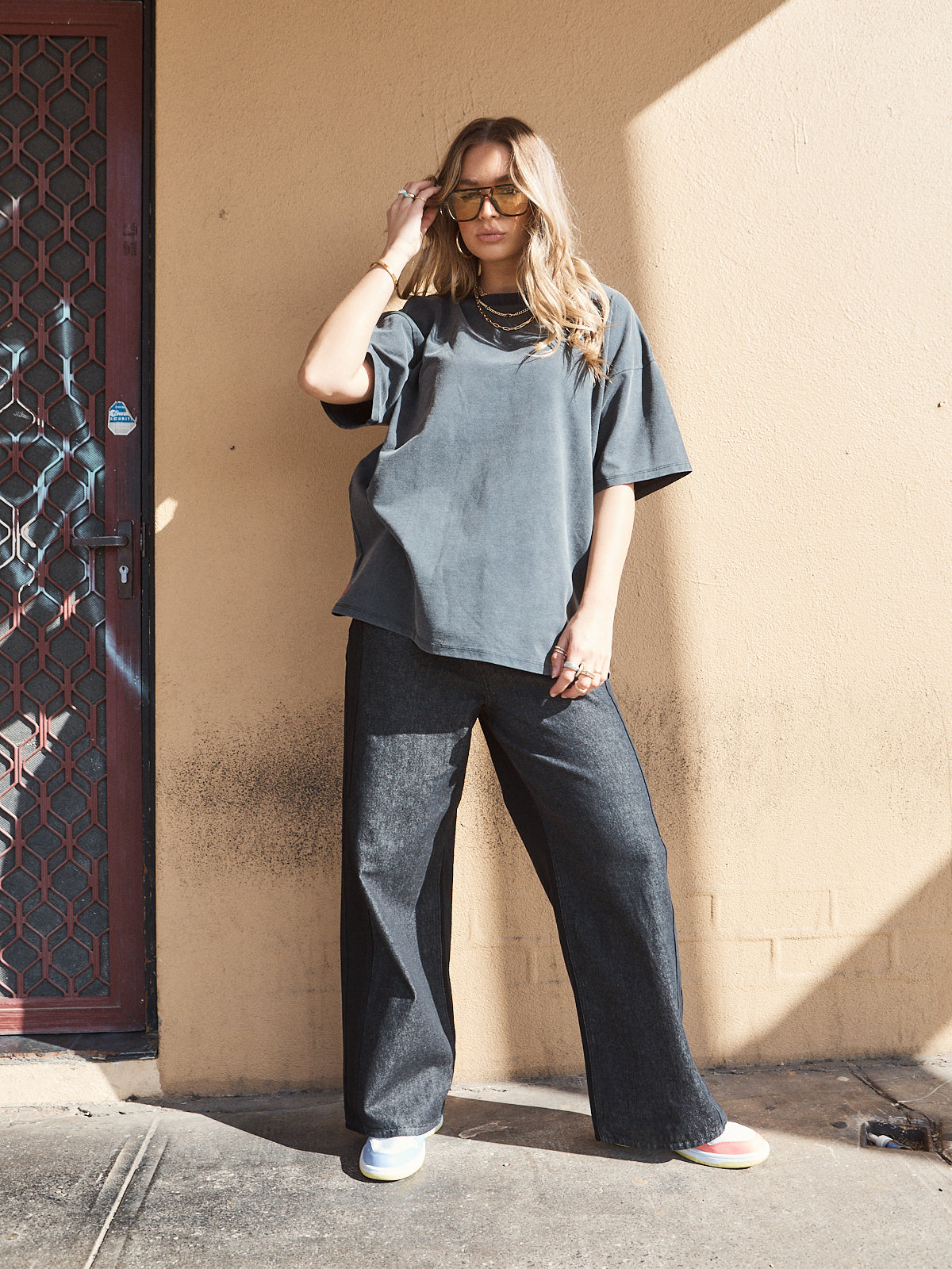 Woman wearing unisex oversized washed black t-shirt styled with wide-leg denim jeans and sneakers.
